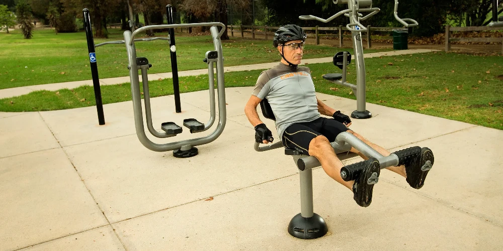 Man using outdoor leg extension machine to strengthen lower body muscles in a park fitness area